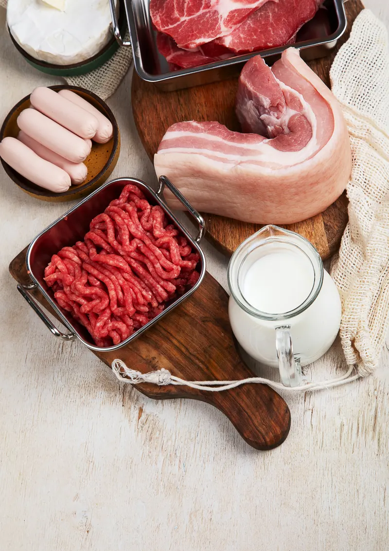Raw beef, sausages, eggs, cheese and a glass of milk on a wooden board: protein ingredients